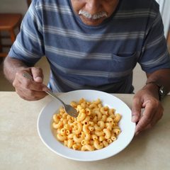 A man in his seventies eating a bowl of macaroni and cheese at a table