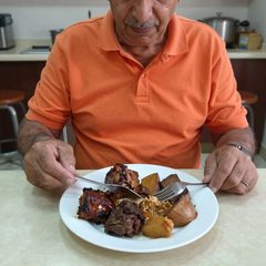 A man in his late sixties eating a plate of roast dinner at a table