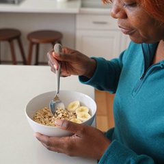 A woman in her seventies eating a bowl of oatmeal with sliced banana at a table