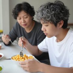 A parent and a teenager eating a bowl of macaroni and cheese at a table