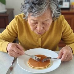 A woman in her seventies eating a plate of pancakes at a table