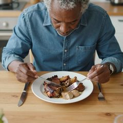 A man in his seventies eating a plate of roast dinner at a table
