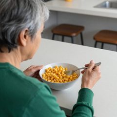 A woman in her sixties eating a bowl of macaroni and cheese at a table