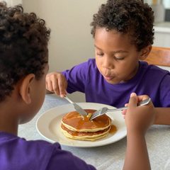 A boy about five years old eating a plate of pancakes at a table
