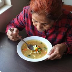 A woman in her late sixties eating a bowl of vegetable soup at a table