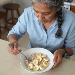 A woman in her seventies eating a bowl of oatmeal with sliced banana at a table