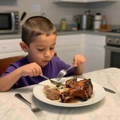 A boy about five years old eating a plate of roast dinner at a table