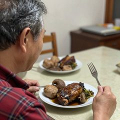A man in his seventies eating a plate of roast dinner at a table