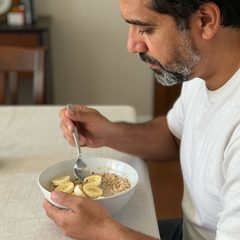 A man about sixty eating a bowl of oatmeal with sliced banana at a table