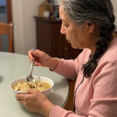 A woman in her seventies eating a bowl of chicken noodle soup at a table