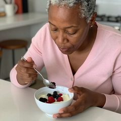 An adult eating lunch alone eating a bowl of yogurt with berries at a table