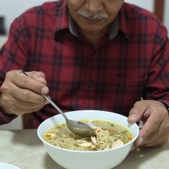 A man about sixty eating a bowl of chicken noodle soup at a table