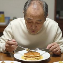 A man in his late sixties eating a plate of pancakes at a table