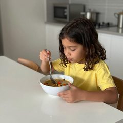 A child about six years old eating a bowl of vegetable soup at a table