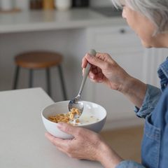 A woman in her late sixties eating a bowl of cereal with milk at a table